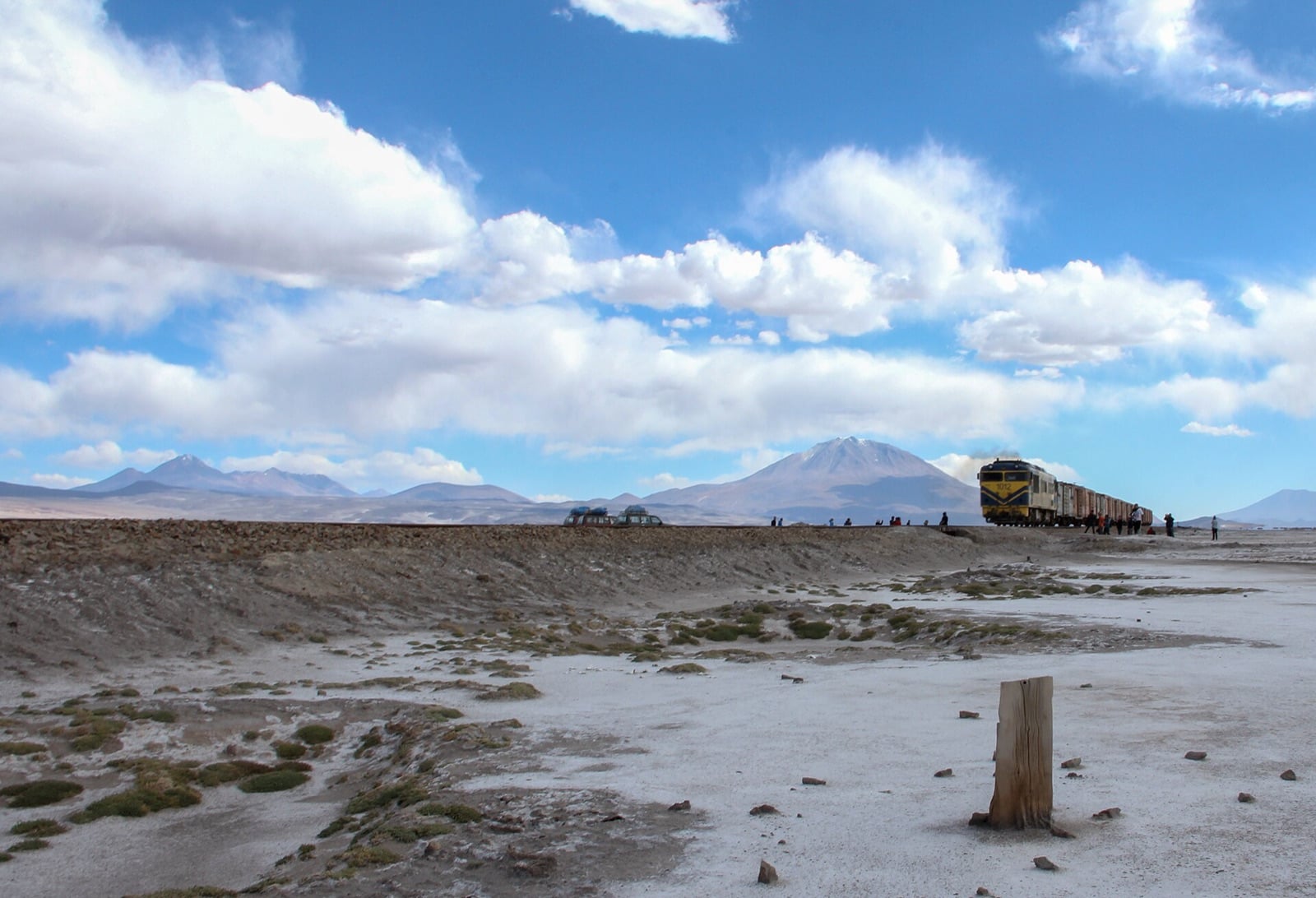 Tren de carga cruzando el Altiplano boliviano con volcanes andinos al fondo
